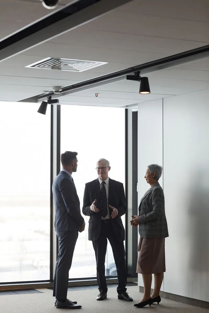 Three colleagues talking by a floor-to-ceiling office window