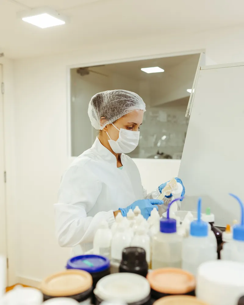 A technician in a hairnet and mask filling containers in a clean room