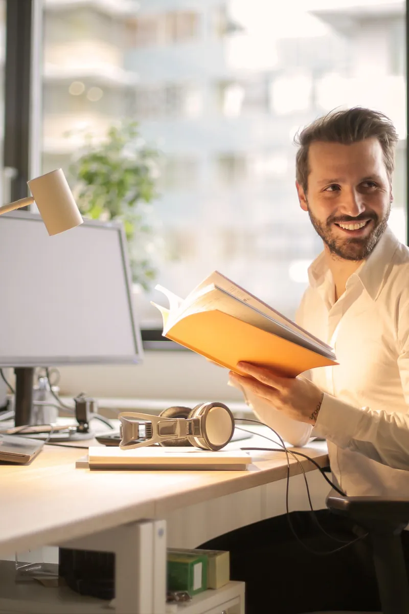 A man reading a folder at a desk with a monitor