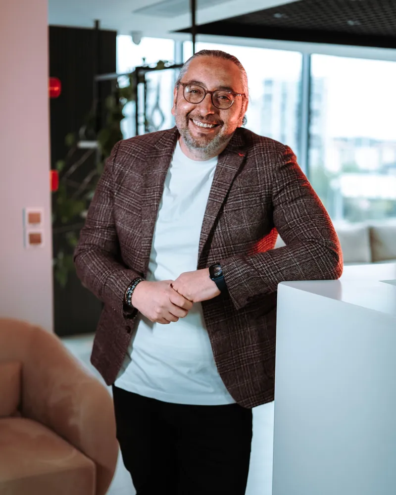 Retrato de un hombre con gafas y americana de cuadros, sonriendo apoyado en un mostrador de una oficina